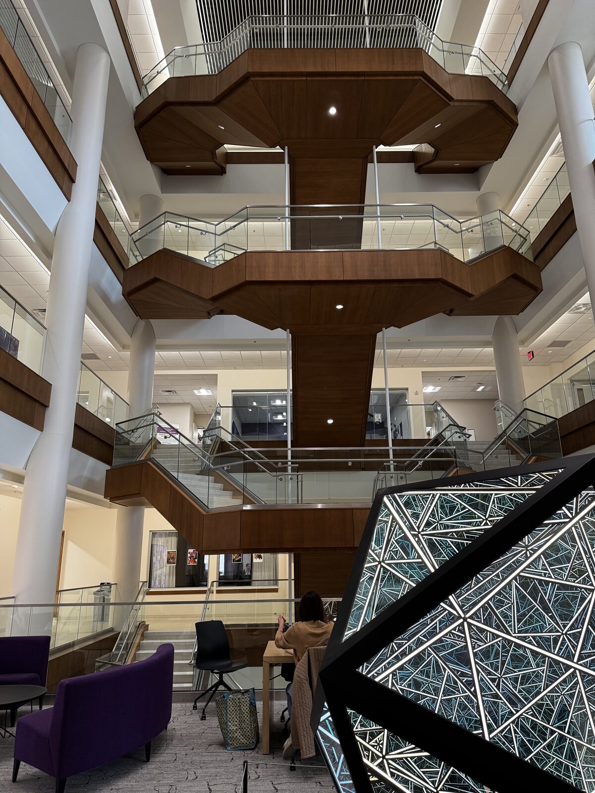 A soaring multi-story atrium at St. Thomas with cantilevered wood balconies and a geometric light sculpture