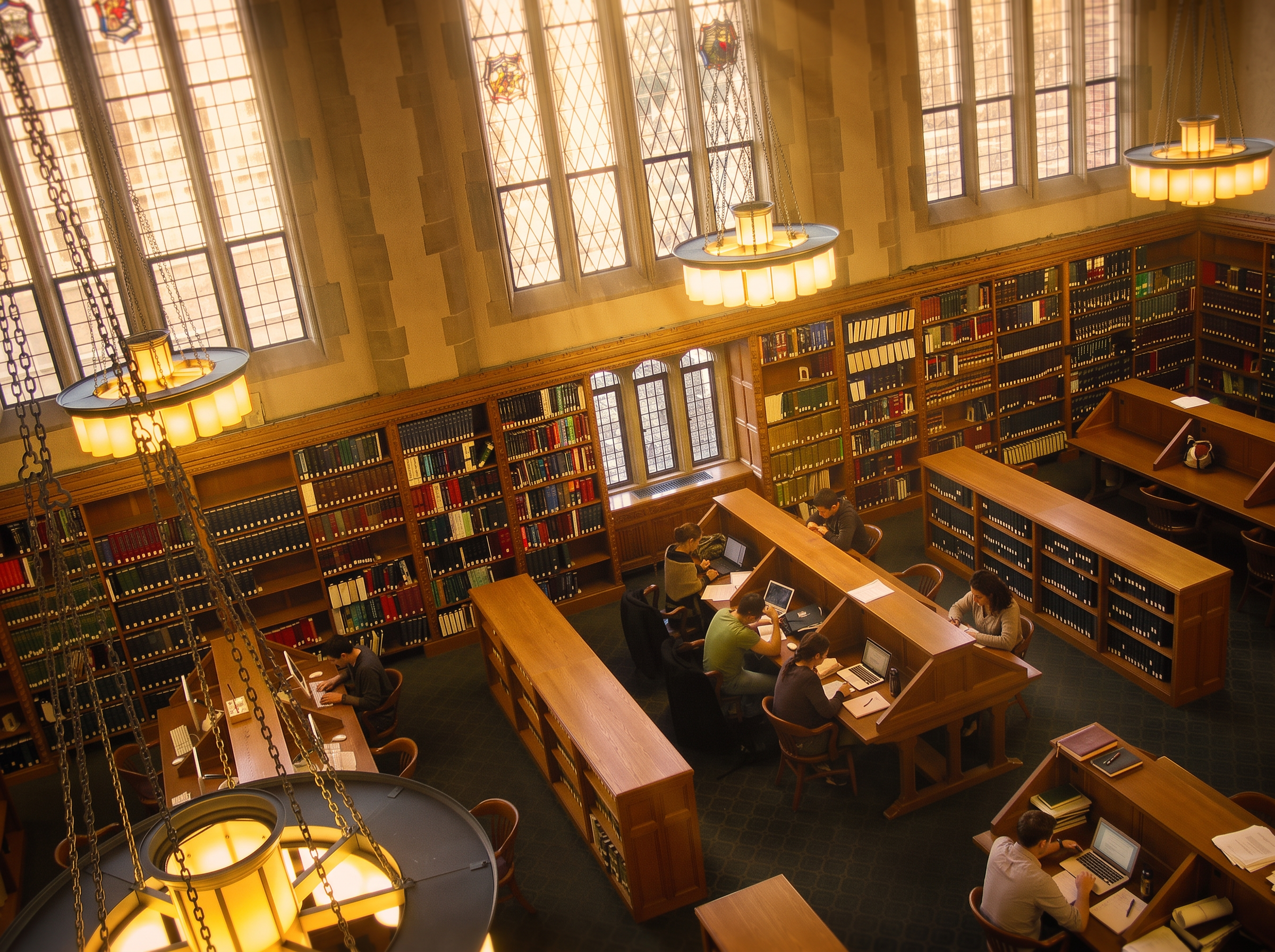 The Yale Law Library reading room, with Gothic windows, glowing lamps, and students studying